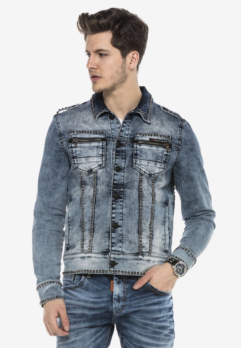 Denimjas in vervaagd blauwe kleur, met zilveren studs, twee borstzakken en knoopsluiting. Voorzien van een klassieke kraag en lange mouwen.