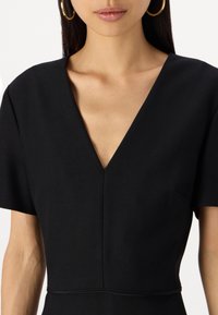 Vestido preto com um decote em V profundo, mangas curtas e uma cintura ajustada. O material parece liso, com costuras mínimas e sem padrões visíveis.