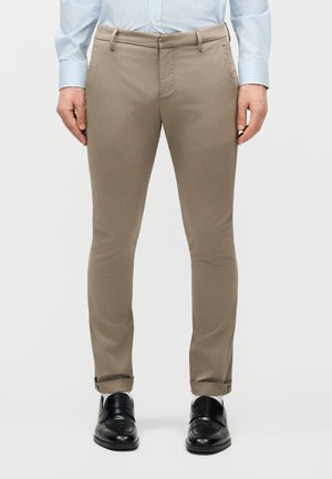 Elölnézet egy személyről, aki bézs színű, karcsúsított nadrágot, világoskék csíkos inget és fekete bőr elegáns cipőt visel.