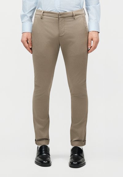 Front view of a person wearing beige slim-fit trousers, a light blue striped shirt, and black leather dress shoes.