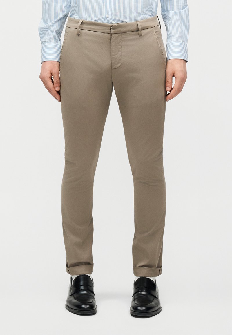 Εμπρόσθια όψη ατόμου που φορά μπεζ παντελόνι στενής γραμμής, ανοιχτό μπλε ριγέ πουκάμισο και μαύρα δερμάτινα παπούτσια φόρμας.