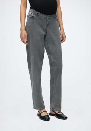 Vrouw draagt een hooggetailleerde vervaagde grijze jeans gecombineerd met een zwart mouwloos topje en zwarte slingbacks met puntige neus, staand op een witte achtergrond.