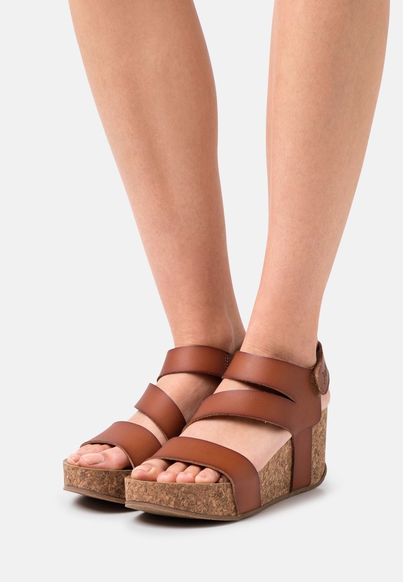 Sandales marron à brides avec un talon compensé en liège, ouverture à l'avant des orteils et bride de cheville ajustable, mettant en valeur une finition en cuir lisse.