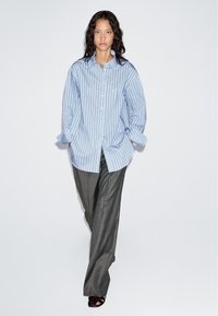 Light blue striped button-up shirt with long sleeves, paired with gray tailored pants and black sandals. Smooth fabric, relaxed fit.