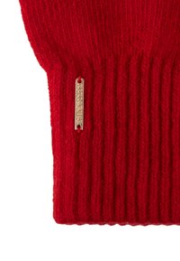 Un pull en tricot rouge avec une texture côtelée et une petite étiquette dorée accrochée sur le côté. Le tissu semble doux et chaud.
