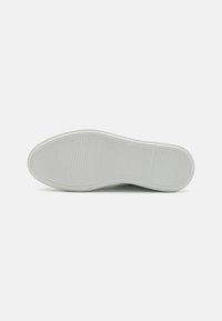 Hvit gummisåle med horisontale og vertikale riller, avrundet tå og glatte kanter, med et lett buet design.
