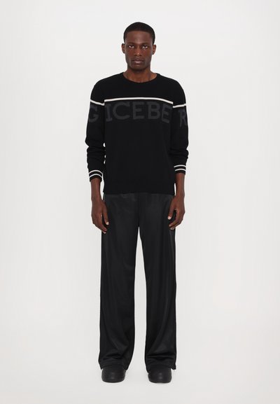 Pull en tricot noir avec des rayures contrastantes plus claires et le texte "ICEBERG". Assorti avec un pantalon large noir et des chaussures noires imposantes.