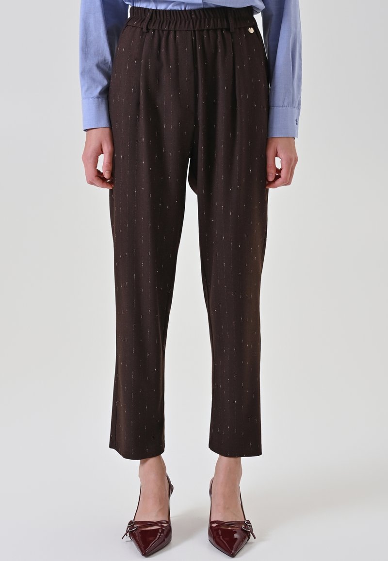 Femme portant un pantalon noir ajusté à fines rayures subtiles, une chemise bleu clair à manches longues, et des escarpins bordeaux à bout pointu.