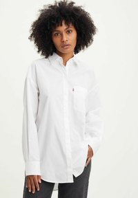 Chemise blanche à manches longues avec un col boutonné, une poche poitrine et une coupe décontractée. Fabriquée en tissu lisse avec un design classique.