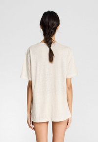 Beige, kortærmet T-shirt lavet af blødt stof. Løs pasform, rund halsudskæring og let længere bagkant. Tekstureret, afslappet design.