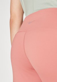 Nike leggingi v breskevni tkanini z gladko teksturo, visokim pasom in subtilno logotipno podrobnostjo. Oblika, ki se prilega, poudari obliko.