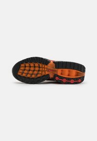 Athletic shoe sole with a black rubber base, orange midsole with circular tread pattern, and red accents. Textured for traction and stability.