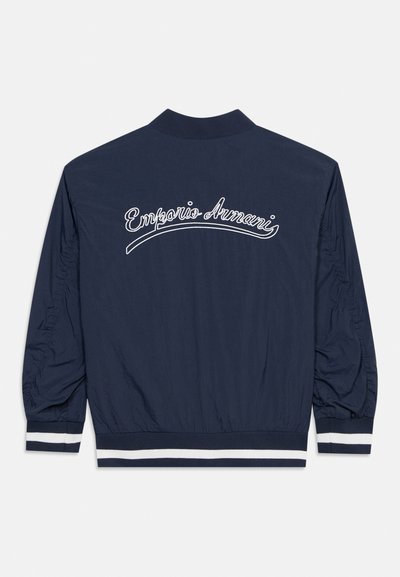Μπουφάν μπόμπερ σε ναυτικό μπλε με μανσέτες και ζώνη μέσης με λευκές ρίγες, με λευκό λογότυπο "Emporio Armani" γραμμένο πάνω στην πίσω πλευρά.