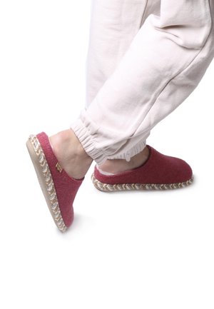 Red felt slip-on shoes with a braided jute sole. Comfortable, rounded shape. Paired with light-colored, elasticated sweatpants.