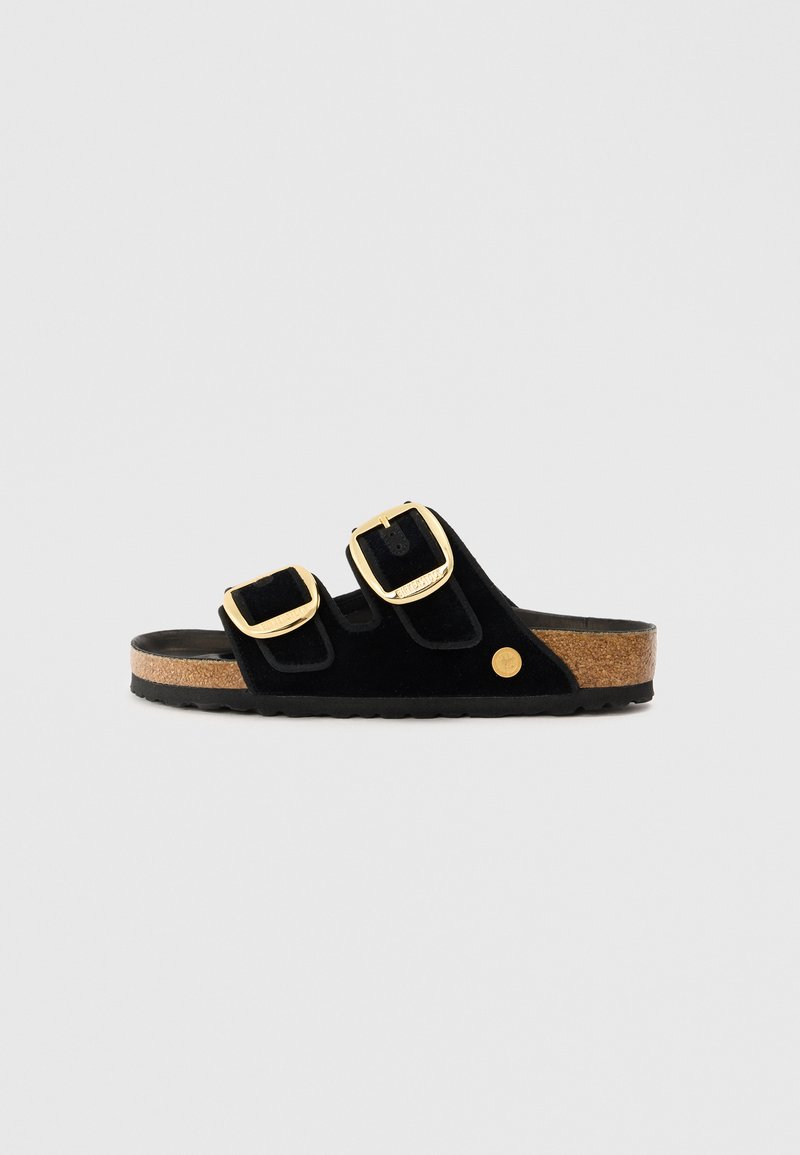 Black suede slide sandal with two gold buckles and a cork footbed. Features a textured black rubber sole and a circular logo accent.