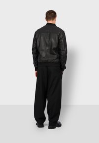 Černá kožená bomber bunda s žebrovaným límcem a manžetami, s hladkou texturou a přiléhavým pasem, nošená přes volné černé kalhoty.