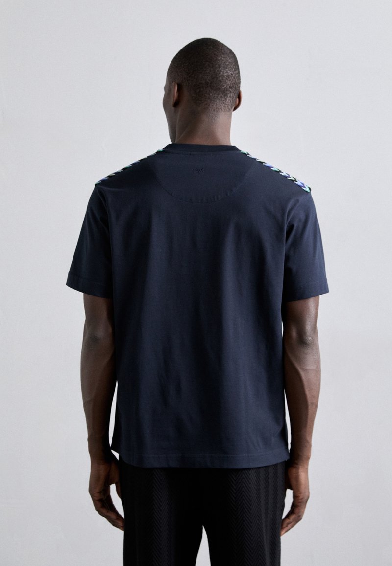 T-shirt en coton bleu marine avec des accents multicolores aux épaules, manches courtes et encolure ronde. Texture lisse, coupe décontractée.