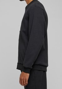 Donkergrijze sweatshirt met lange mouwen, een ronde halslijn, ribgebreide manchetten en zoom, en een zichtbare zijzak. Zachte textuur en eenvoudig ontwerp.