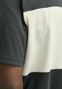 Camiseta de manga corta con un diseño en bloques de color en gris oscuro y crema, hecha de algodón suave, con detalles de costura visibles.