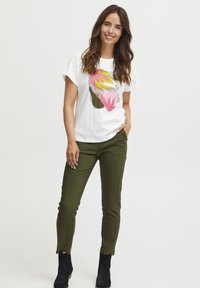 Valge puuvillane T-särk värvilise lillegraafikaga. Oliivrohelised kitsad püksid külgõmblustega. Mustad pahkluu saapad. Lihtne, modernne disain.