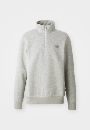 Grå sweatshirt med høj krave, kvart lynlås foran og ribbede ærmer. Har et lille logo patch på venstre bryst.