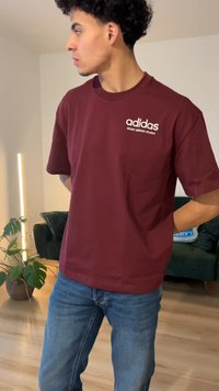 Vīnu sarkana kokvilnas T-krekls ar apaļu kaklu un īsām piedurknēm, uz kura redzams balts Adidas zīmols un uzraksts "SPORT DESIGN STUDIO".