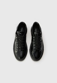 Sapatilhas pretas em couro brilhante com acabamento suave, bico redondo e atacadores pretos. Solas texturizadas com design minimalista.