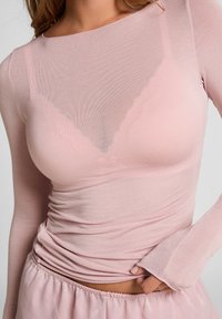 Lichtroze langharige top met een ronde halslijn en textuurstretch stof, met geplooide details bij de taille en duimgaten bij de manchetten.