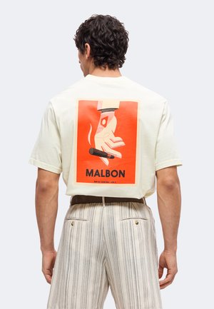 Mand iført hvid t-shirt med orange grafik af en hånd, der holder en cigar, og ordet "MALBON" på ryggen, kombineret med stripede bukser.