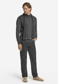 Grauer gestrickter Pullover mit einem über die Schultern gelegten Schal, kombiniert mit dunkelgrauen Hosen und beige Schuhen. Glatte Textur und einfaches Design.