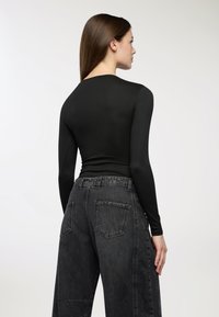 Czarna bluzka z długim rękawem o dopasowanym kroju, zestawiona z ciemnoszarymi, luźnymi dżinsami o wysokim stanie z tylnymi kieszeniami.