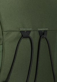 Dunkelgrüner, strukturierter Stoff mit zwei schwarzen elastischen Schlaufen, die an schwarzen Nähtelementen befestigt sind.