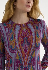 Többszínű, hosszúujjú felső, amely bonyolult paisley mintázattal rendelkezik lila, sárga és Türkiz színben egy texturált szürke háttérrel.