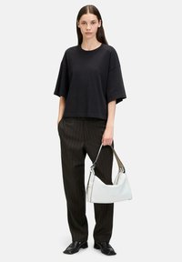 Czarny, oversize t-shirt z krótkim rękawem, w połączeniu z spodniami w paski. Model trzyma białą, zakrzywioną torbę, która ma czarny akcent.