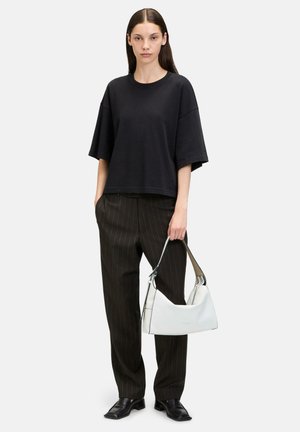 T-shirt noir oversize à manches courtes, associé à un pantalon à rayures. Le modèle tient un sac à main courbé blanc avec un accent noir.