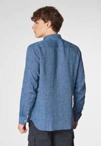 Camicia in chambray blu a maniche lunghe con colletto bottonato, texture sottile e orlo arrotondato, dotata di polsini con bottoni e vestibilità rilassata.