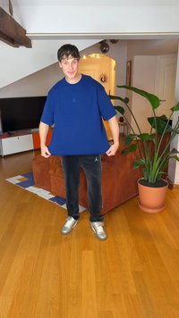 Modré volné tričko s logem Jordan, černé tepláky s modrými akcenty a stříbrné tenisky, zasazené do vnitřního obytného prostoru.