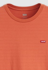 Oranžinė trumpomis rankovėmis marškinėliai su horizontaliai įribuotu paviršiumi, apvaliu iškirpimu ir mažu raudonu Levi's logotipu kairėje krūtinės pusėje. Pagaminti iš medvilnės.