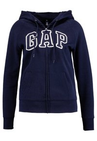 Sudadera con cremallera de color azul marino, con letras en blanco "GAP", capucha con cordón, puños acanalados y bolsillos delanteros; fabricada en suave material de felpa.