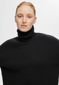 Črn pulover s turtleneck i značajem labavog in prevelikega kroja. Narejen je iz mehkega blaga, ima riban ovratnik in gladko teksturo.