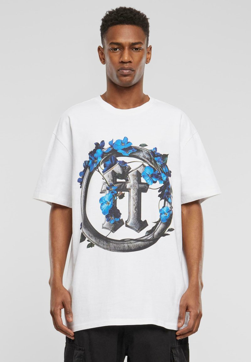 Hvit oversized t-skjorte med et fargerikt grafisk design av et kors omgitt av blå blomster og grønne blader. Korte ermer, rund hals.