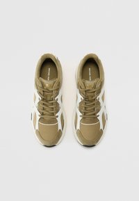Grønne og hvite sneakers med en blanding av stoff og syntetiske materialer, med et teksturert design og gullakzent på logoen.