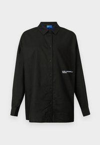 Camisa negra de botones con collar clásico, mangas largas y un logo bordado en el lado izquierdo. Fabricada con tela suave.