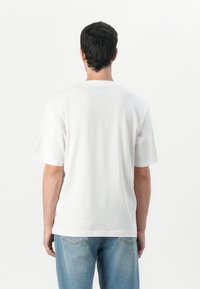 Camiseta de algodón blanca con cuello redondo, mangas cortas y un corte relajado, combinada con jeans de mezclilla azul claro. Diseño minimalista, textura suave.