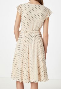 Beige klänning med korta volangärmar, med ett prickigt mönster i brunt. Utställd kjol med en åtdragen midja och mjuka veck.