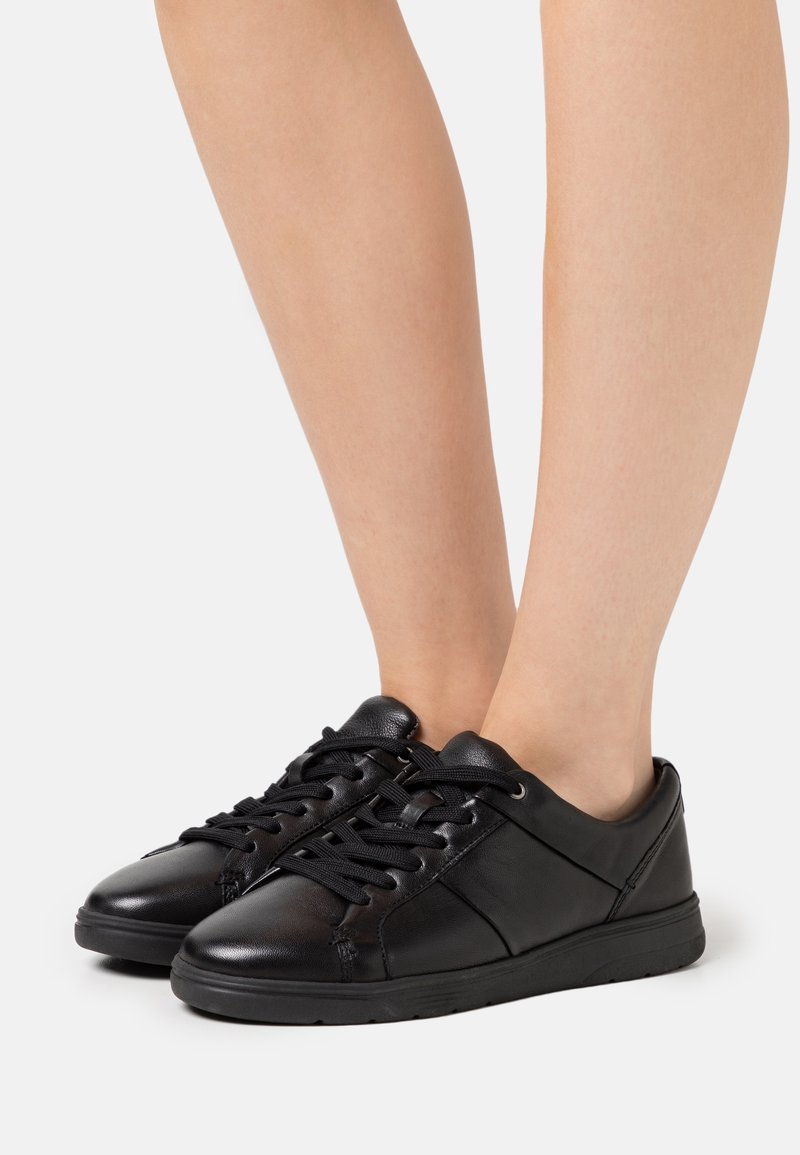 Mustat nahkakengät, joissa on sileä pinta, pyöreä varvas ja litteä kumipohja. Ominaisuuksiin kuuluu kontrastoiva ompelu ja perinteinen nauhakiristys.