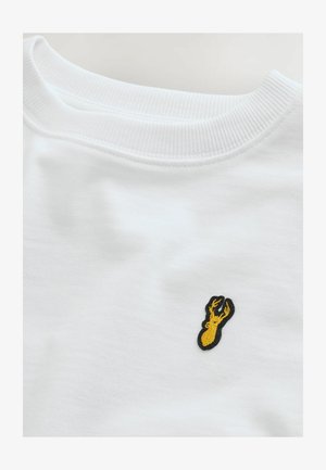 Bela pulover s strukturo na vratu in majhnim, črnim vezenim motivom jastreba v rumeni barvi na prsih. Mehka tekstura po celotni površini.