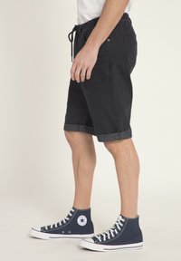 Pantalones cortos de denim negro con puños enrollados, que cuentan con una cinturilla elástica y cordón. Combinados con zapatillas de alta tops en azul marino.