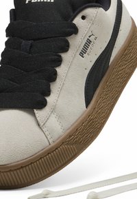 PUMA velúr sneaker, bézs felsőrésszel, fekete részletekkel, vastag fekete fűzőkkel és textúrált barna gumitalppal. Extra fehér fűzők is tartoznak hozzá.