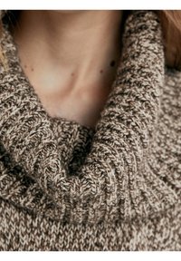 Pull tricoté marron avec un col roulé épais. Le motif texturé présente des fils alternés clairs et foncés, accentuant la chaleur du matériau.